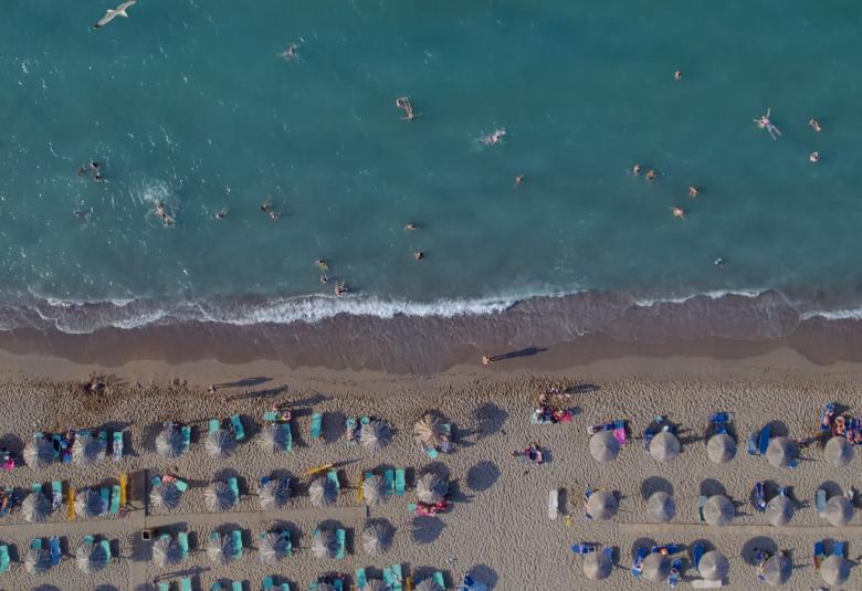 Kuvassa on sinistä merta ja ihmisiä aurinkotuoleissa ylhäältä päin kuvattuna. 