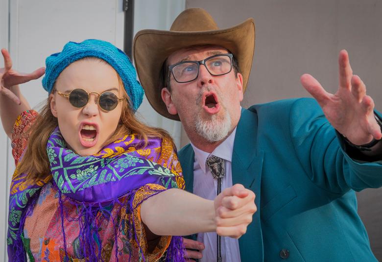 Kuvassa on puolivartalokuvassa nuori nainen ja mies.  Heillä on vasen käsi edessä ja oikea käsi takana ojennettuina.  Naisella on värikkäät vaatteet ja turkoosi baskeri.  Miehellä on stetson.