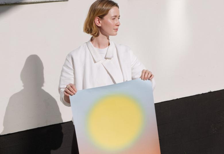 Kuvassa on Anna Smeck, joka pitää edessään julistetta, jossa on iso keltainen pyöreä aurinko.