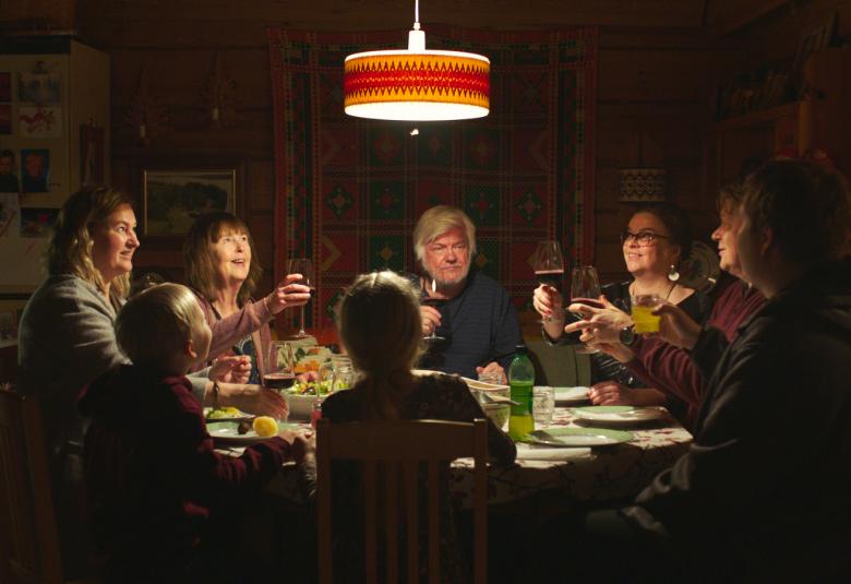 Kuvassa ovat Riia Kataja, Leena Uotila, Tom Wenzel, Elina Knihtilä ja Jarkko Pajunen syömässä joulupöydän ääressä.  Pöydällä on ruokaa ja valaistus on tummahko keltavaloinen.