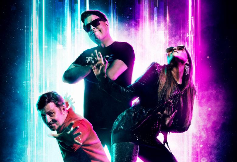 Kuvassa ovat Aikakoneen kolme jäsentä asetelmassa, jossa vasemmalla on mies puolittain kumartuneena toinen mies keskellä ojentuneena, Oikealla on nainen leuka ylöspäin. Tausta on tumma.