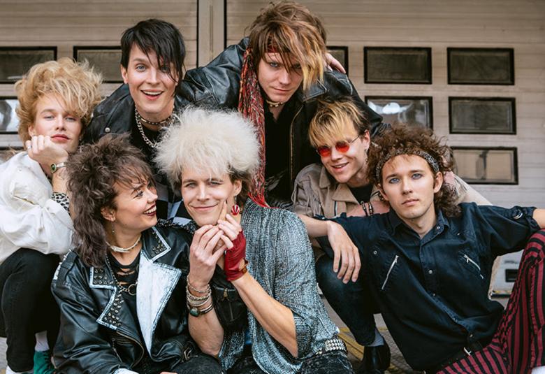 Kuvassa ovat Dingon näyttelijät,  jotka istuvat lattialla yhtenäisenä ryhmänä. Heillä pitkähköt hiukset ja mustat tai vaaleat pusakat päällään.