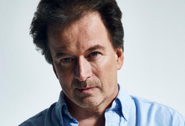 Kuvassa on Kjell Westö kasvokuvassa ja hänellä on vaalean sininen paita päällään.