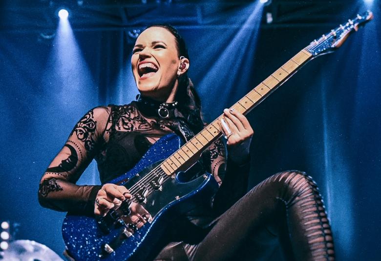 Kuvassa on Erja Lyytinen soittamassa kitaraa ja kuva on otettu yläviistoon.  Hänellä on musta läpikuultava puku, jossa on kukallista ja ruotomaista kuviointia. Kuvan sävy on tumman sininen sävy ja taustalla on kohdevaloja.