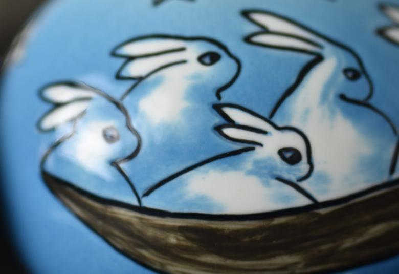 Kuvassa on Helinä Liukko-Sundströmin valkoisia jäniksiä menossa oikealle sinisellä pohjalla ja ruskeassa veneessä.