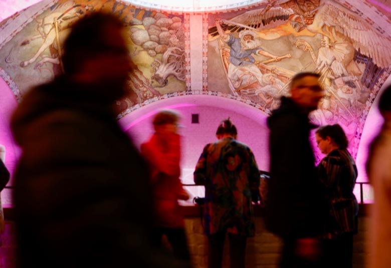 Kuvassa on Kansallismuseon aula, jossa liikkuu paljon ihmisiä.  Kuvassa näkyy pinkkiä kattoa, jossa on freskoja.