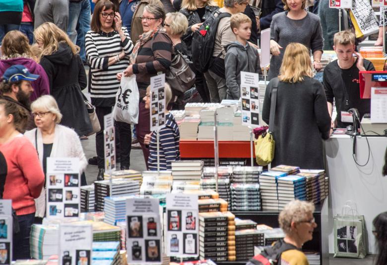 Kuvassa on ihmisiä katselemassa kirjoja, joita on isolla pöydällä Kirjamessuilla Messukeskuksessa.