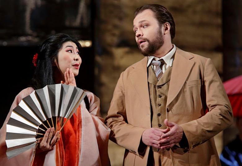 Kuvassa ovat Hye-Youn Lee roosan värisessä mekossa, punaisessa huivissa ja oikeassa kädessään hopean värinen viuhka.  Vieressä oikealla on Mika Pohjonen vaalean ruskassa puvussa. 