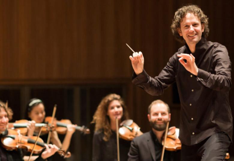 Kuvassa on Nicholas Colon oikealla johtamassa orkesteria ja vasemmalla näkyy joitakin soittajia.