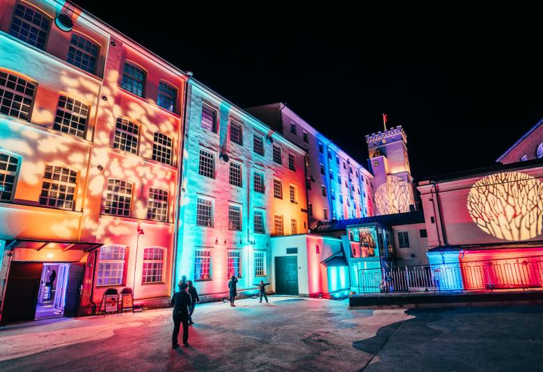 Kuvassa on Finlaysonin alueella värikkäät seinät ympäri aukiota. Oikealla seinällä on pyöreä kullan värinen kuvio. 