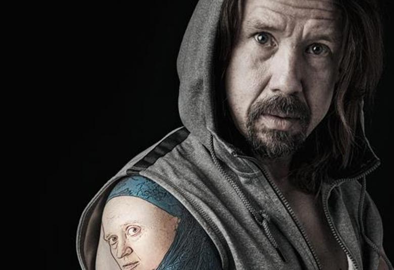 Kuvassa on Tommi Eronen vinottain kuvan oikeassa laidassa.  Erosella on päällään harmaa, hihaton huppari ja oikeassa kädessään olkapäästä alaspäin tatuointi. Siinä on nuorem miehen kasvojen kuva.