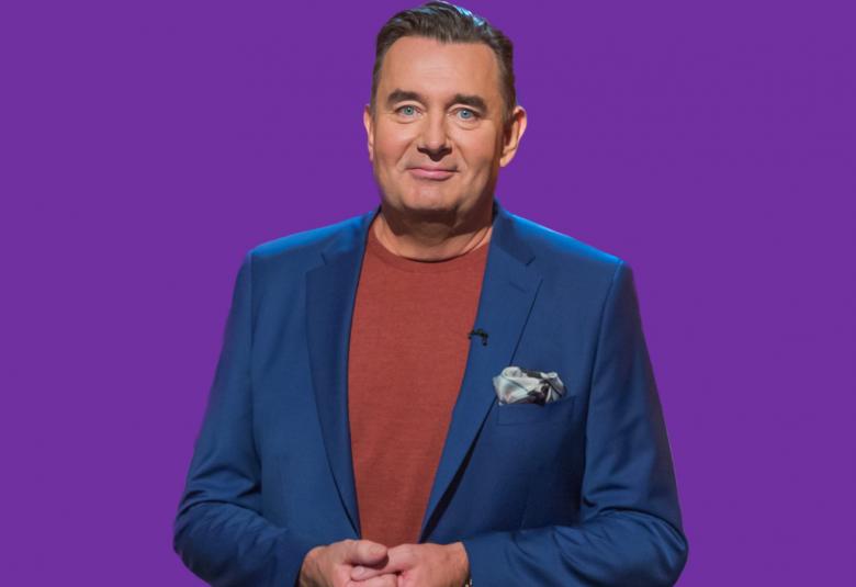 Kuvassa on Timo Koivusalo seiromassa ja hänellä on sini-turkokosi takki ja ruosteen ruskea t-paita. Tausta on lila.