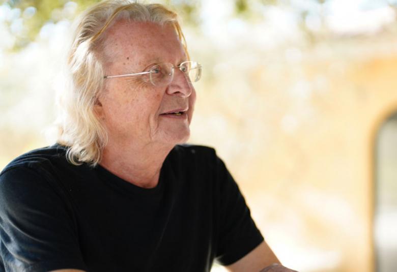 Kuvassa on Tristan Murail istumassa vinottain oikealle.  Hänellä on vaaleat hiukset ja musta t-paita. Taustalla näkyy himmeästi vihreää puustoa ja keltaisen muurin aukko.