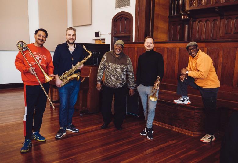 Kuvassa ovat soittajat Delfeayo Marsalis, Timo Lassy, Kirk Joseph, Jukka Eskola, Herlin Riley rennosti rivissä, joista viimeinen on nostanut oikean jalkansa urkujen penkille ja nojaa kädellään reiteensä.  Salissa on tumma lattia ja seinän vieressä olevat kaapistot ja paneelit ovat tummaa puuta.