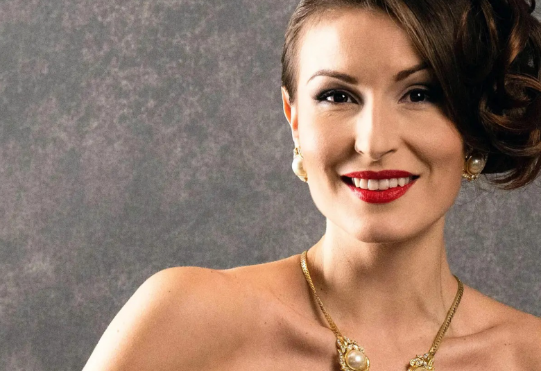 Kuvassa on Maria Lund, jolla on tummat, pitkät hiukset vasemmalle koottuna kiharaiseksi kampaukseksi. 