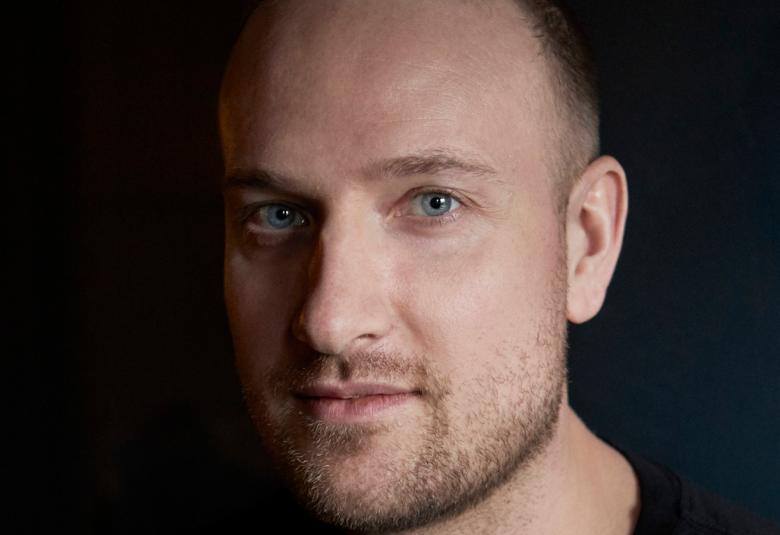 Kuvassa on Max Seeckin kasvokuva ja vasemmalla on osassa kasvoja himmennystä. Tausta on tumma. 