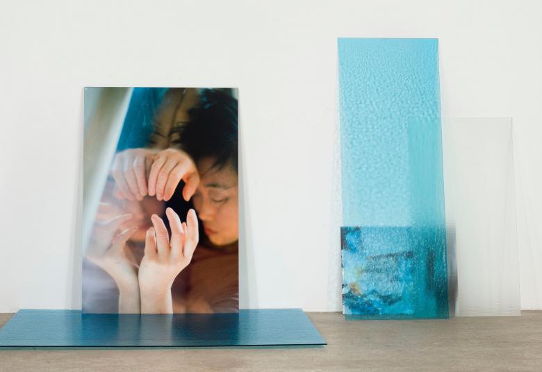 Kuvassa on vasemmalla on lattialla olevan levyn takana teos, jossa on naisen kasvot ja hänpitelee vaalean ruskeaa palloa.  Vieressä on kapean vaalean sininen teos.