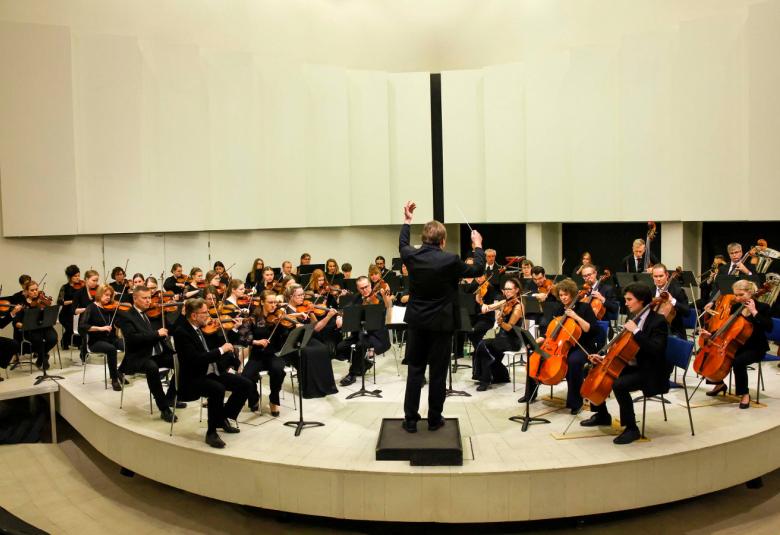 Kuvassa on Tampereen sinfoniaorkesteri kaaressa esiintymislavalla, joka on vaaleaa puuta.
