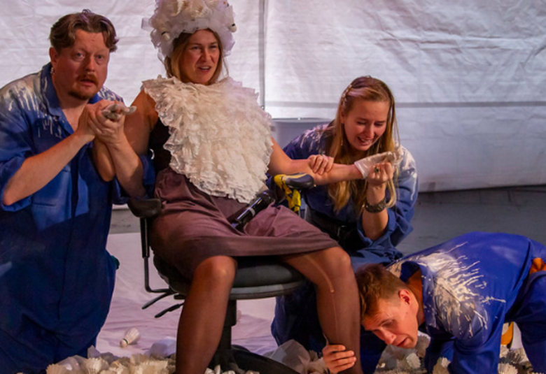 Kuvassa on vasemmalla mies sinisessä paidassa polvillaan ja nainen istumassa tuolilla valkoisessa röyhelöperuukissa ja kaulurissa.  Hänen vieressään on polvillaan lattialla nainen ja hän pitää toista naista vasemmasta kädestä. Edessä on mies kumartuneena maahan, jossa on roskaa.