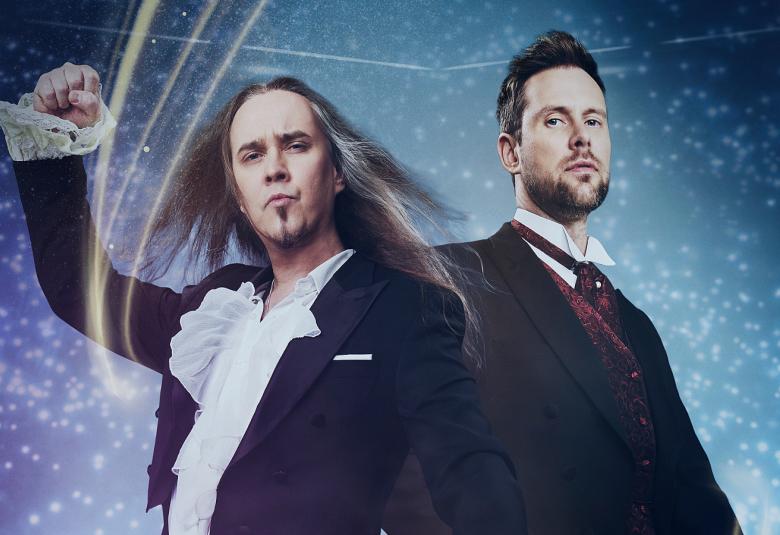 Kuvassa ovat Jarkko Ahola ja Waltteri Torikka.  Vasemmalla on Aholalla on oikea käsi pystyssä ja siihen osuu kolme valojuovaa.  Torikka seisoo sivuittain Aholaan nähden. Heillä on mustat frakit päällään. Taustalla on erilaisia sinisiä. 