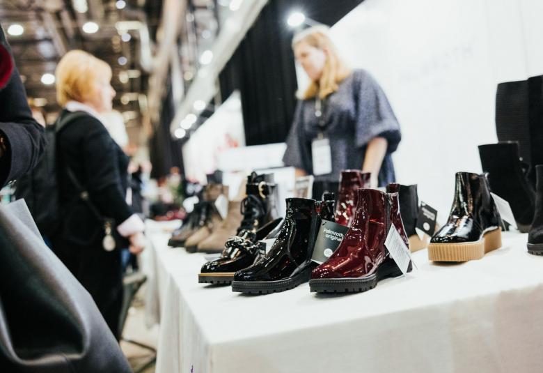 Kuvassa on näyttelypöydällä eri värisiä nilkkakenkilä. Taustalla näkyy eisttelijä ja vastapäätä pöydän toisella puolella asiakas.