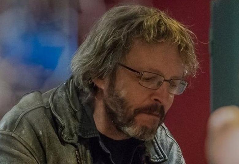 Kuvassa on Hannu Paloviita istumassa sivuttain katse oikealle. Hänellä melko pitkät taipuisat hiukset ja hänellä on ruskeaä nahkatakki päällään. Hänellä on partaa. Taustalla on ruskeaa ja sinistä. Kuva on puolivartalokuva.