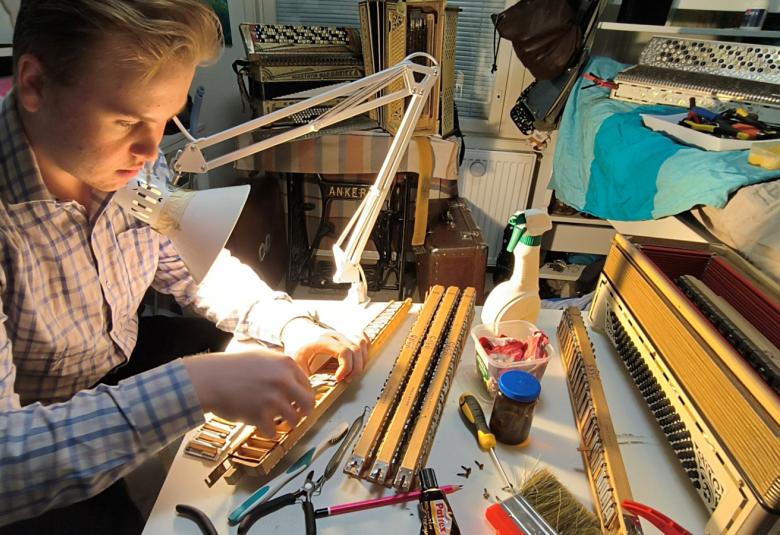 Kuvassa on Petu Partanen pöydän ääressä pöydän ääressä harmonikkaa.  Kuva on otettu yläviistosta. 