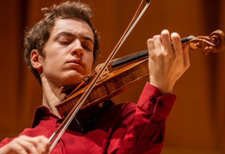 Kuvassa on Adrian Ibañez-Resja soittamassa viulua ja hänellä on punainen paita päällään.  Kuva on puolivartalokuva. Tausta on ruskea.