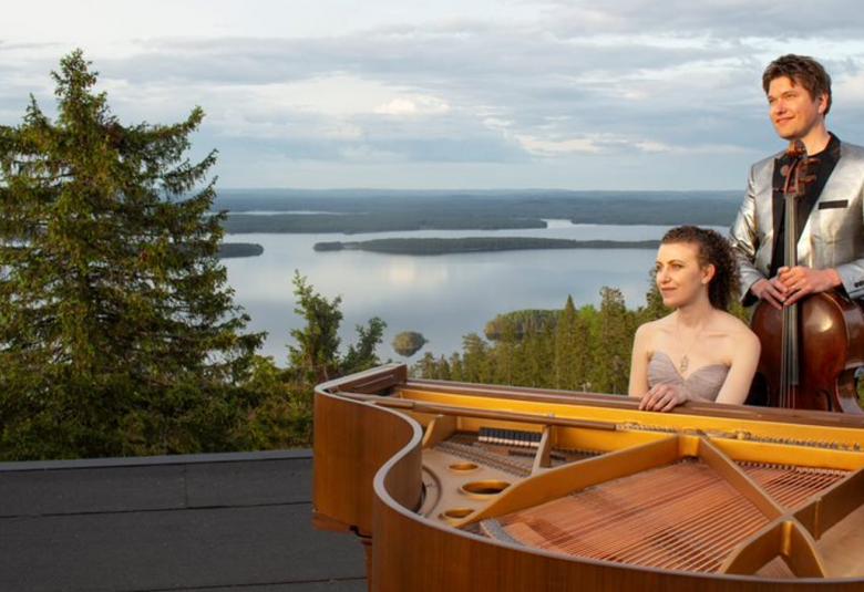 Kuvassa ovat ruskean flyygelin takana Nazig Azezian istumassa ja Jussi Makkonen seisomassa. Taustalla on Kolin kesämaisema järvineen ja saarineen.