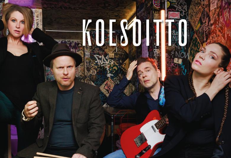 Kuvassa on istumassa sohvalla vasemmalla nuori nainen mustissa vaatteissa, sohvalla alempana mies mustassa lierihatussa ja vieressä on nuori mies punainen kitara sylissään.  Hänen edessään on nuori nainen, joka laittaa korvakorua vasempaan korvaansa.