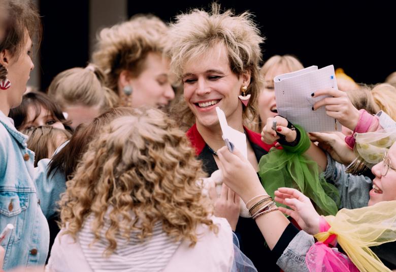 Kuvassa on keskellä Alvari Stenbäck ihailijoidensa keskellä ja häneltä pyydetään nimikirjoituksia.  Kuvassa näkyy nuorten tyttöjen päitä ja käsiä ojentamassa papereita.