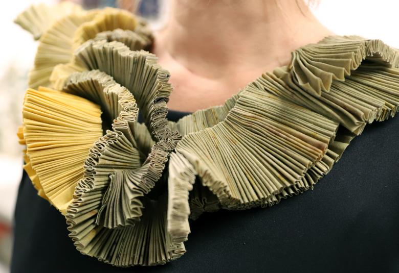 Kuvassa on mustanpuvun kaulus, jossa on kierteisesti vaalean ja sammaleen vihreän värillä kierteinen runsas kaulakoriste kankaasta.