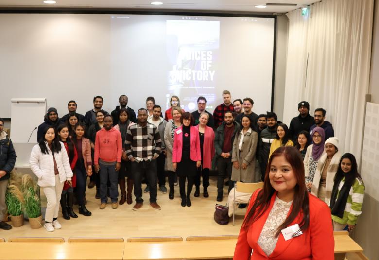 Kuvassa ovat avajaistilaisuuden osallistujat yhteiskuvassa kokoustilan seinän vieressä ja heitä on noin 40.  Etualalla seisoo Rozabela Singh punaisessa jakussa.  