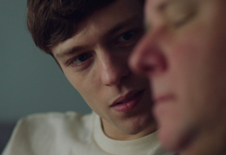 Kuvassa on kasvokuvassa Sebastiania esittävä nuori miesnäyttelijä, joka katsoo vieressään olevaa miestä. Vieressä oleva mies on sivuttain ja hänet on himmennetty. 