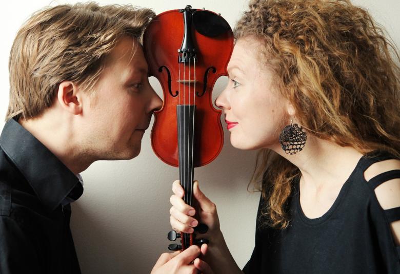 Kuvassa ovat Antti Tikkanen v. Takaa asemmalla ja Minna Pensola oikealla puolivartalokuvassa.  He pitävät välissään käsissään viulua varresta kiinni ylösalaisin.