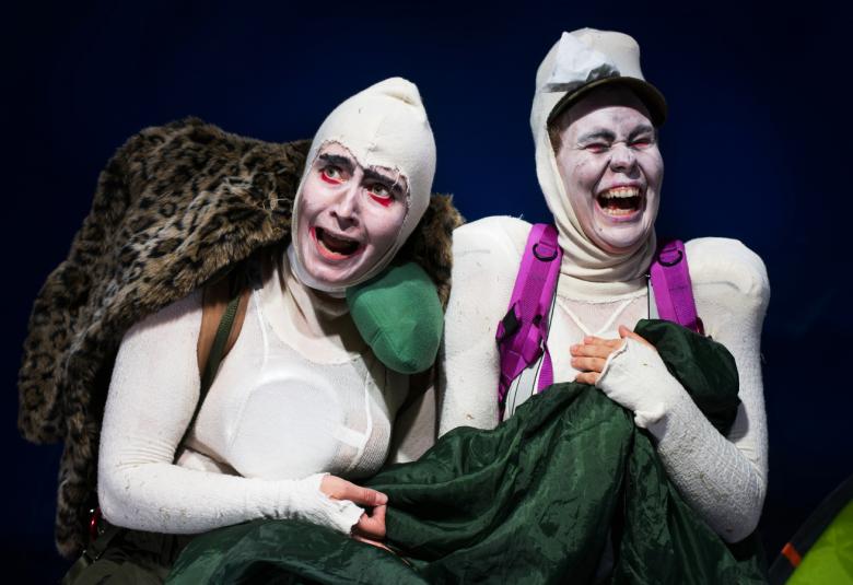 Kuvassa on vaaleat sukkapuvut ja päässään myös vaaleat huput. Heillä on tumma peitto käsissään.