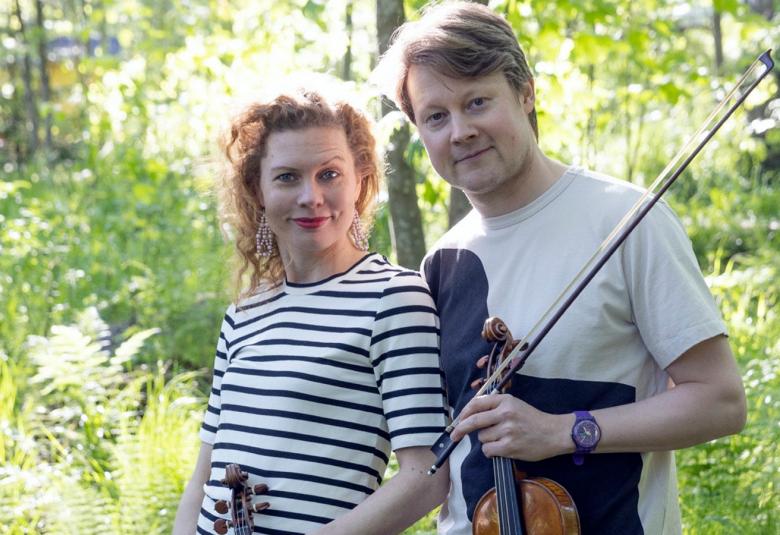Kuvassa ovat Minna Pensola musta-valko raidallisessa puserossa ja Antti Tikkanen valkoisessa t-paidassa viulu kädessään.  He ovat lehtomaisessa, vihreässä metsässä.