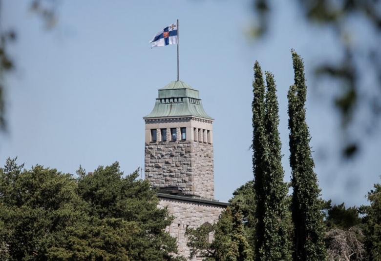 Kuvassa on Kultarannan päärakennuksen yläosan torni harmaasta kivestä.  Siinä liehuu Suomen virallinen lippu. Kuva on kesäkuva ja vieressä oikealla korkeita tuijia. Vasemmalla matalampia lehtipuiden latvoja.