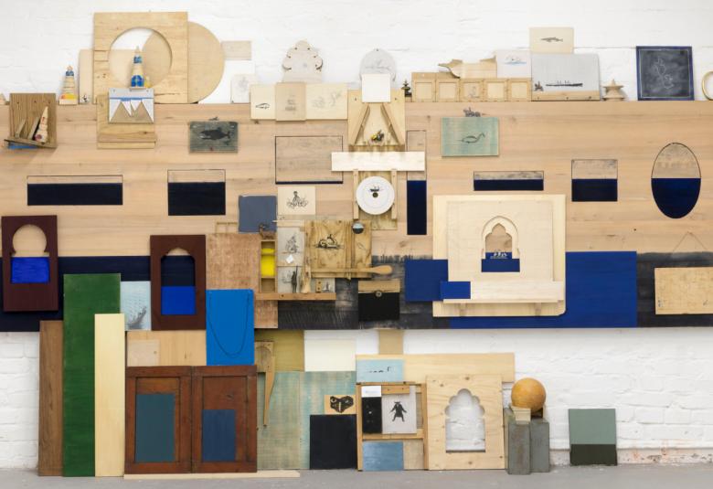 Kuvassa on puusta tehty hiukan taloa muistuttava puupalikoista koottu muodostelma.  Siinä on erilaisia pueniä elementtejä eri palikoissa, mm. kompassi, kello, tiimalasi jne. Yläosassa on enemmän vaaleata puuta ja alaosassa tummaa.