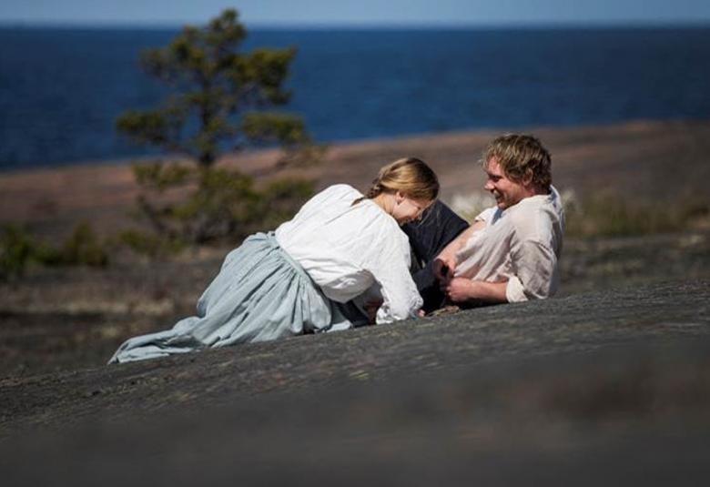 Kuvassa ovat Amanda Jansson ja Linus Troedsson makailemassa rantakalliolla meren äärellä.  Jansson on kääntyneenä Troedssonin suuntaan ja hänellä on valkoinen pusero ja vaalean sininen hame päällään. 