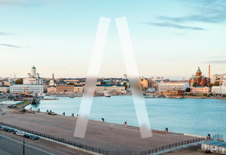 Kuvassa on näkymä kauppatorin suuntaan ja etualalla on asfalttinen parkkipaikka ja takana merenlahtea.  Taustalla mm. Helsingin tuomiokirkko ja ympäröiviä rakennuksia. Taivas on sininen. Taivaalta tulee kaksi vaaleaa palkkia, jotka osoittavat kohti tonttia A-kirjaimen muotoisesti ilman väliviivaa.