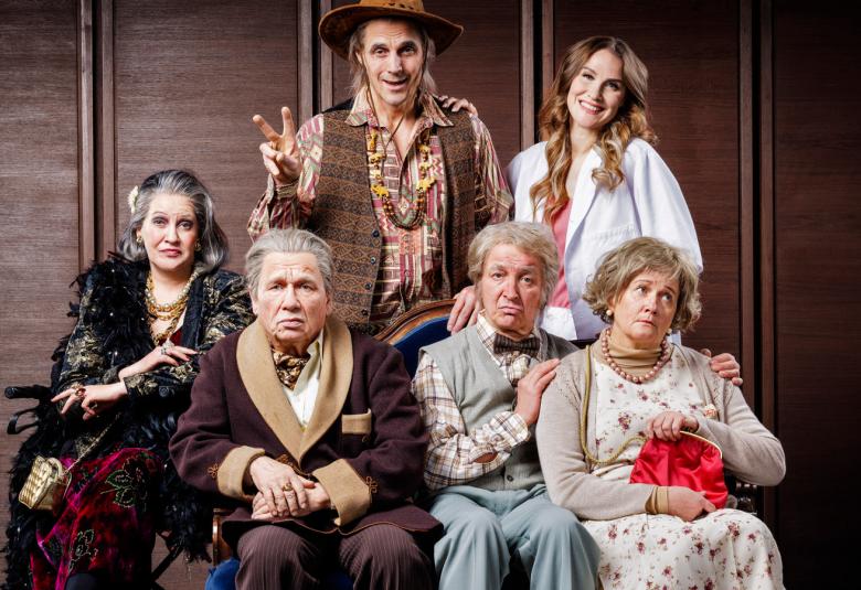 Kuvassa on neljä näyttelijää alarivissä istumassa ja kaksi ylärivissä seisomassa. He ovat vanhojen ihmisten vaatteissa.