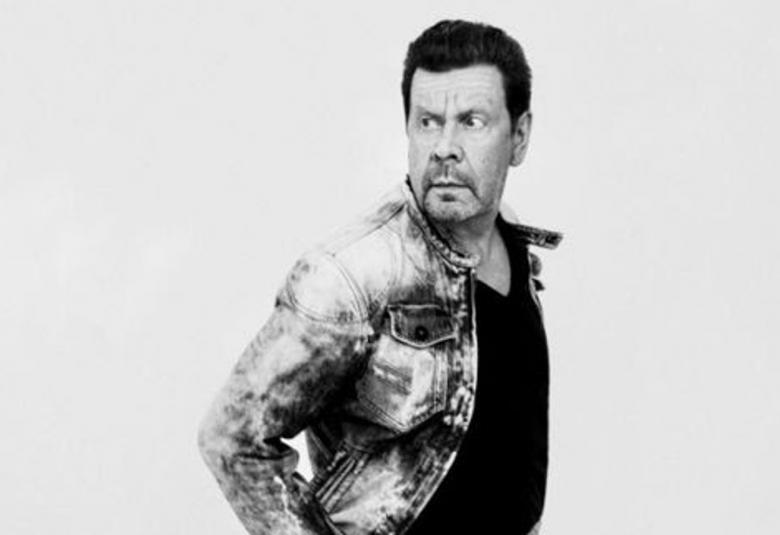 Kuvassa on Pate Mustajärvi farkkutakissa ja hän on vinottain ja katse taaksepäin. Kuva on musta-valkoinen.