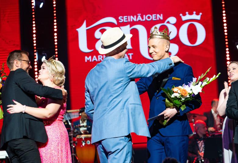 Kuvassa on menossa Tangomarkkinoiden voittajien onnittelut ja kukitus. Vasemmalla on Charlotta Saaren onnittelu ja halaus.  Hänellä on pinkki puku päällään.  Vieressä on Pasi Flodströmin onnittelut ja onnittelijalla on vaalean sininen puku.  Tausta on punainen ja seinällä lukee tango.