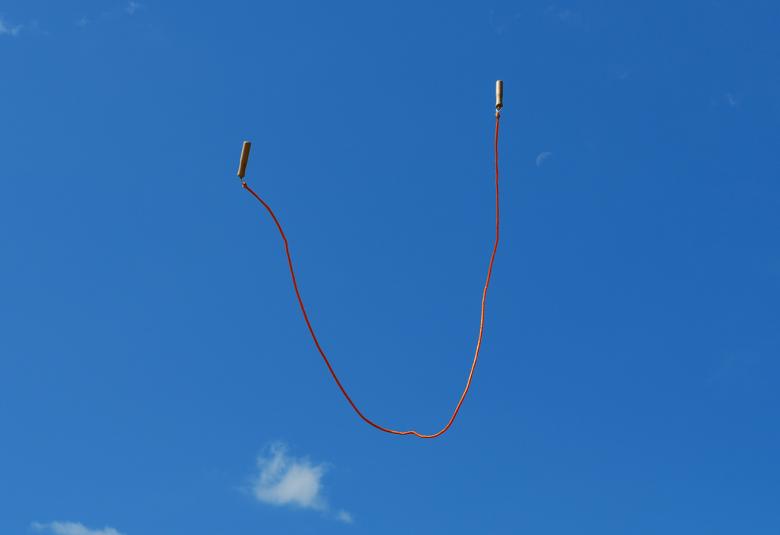 Kuvassa on hyppynaru leijumassa sinistä taivasta vasten ja alhaalla on pari pientä poutapilveä.