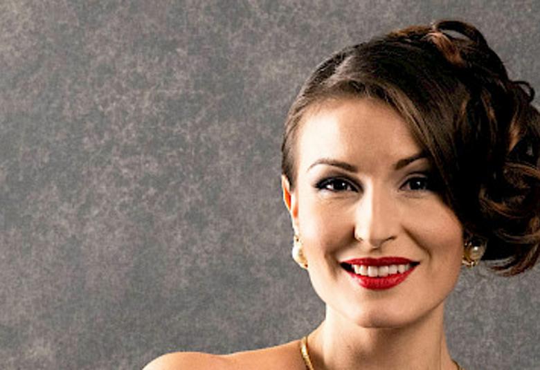 Kuvassa on Maria Lund kasvokuvassa.  Hänellä on avonainen olkaimeton kaula-aukko ja hnen hiuksensa on kammattu ylös ja on kiharalla vasemmalla puolella. Kaulassa on vaaleans ruskea koru. Tausta on harmaa.