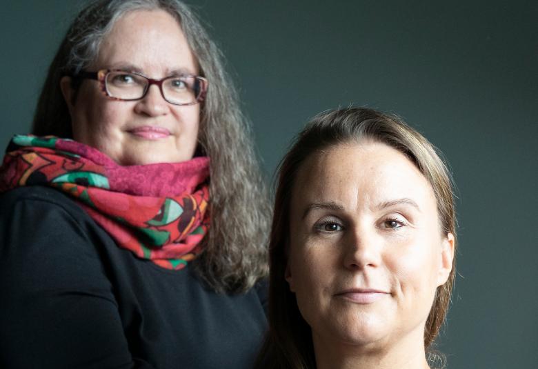 Kuvassa on vasemmalla ylempänä Stella Vuoma mustassa mekossa ja punaisessa huivissa. Hänellä on pitkät, kiharat hiukset. Oikealla alempana istuu Saana Kiviranta kasvokuvassa. Tausta on tumman harmaa.