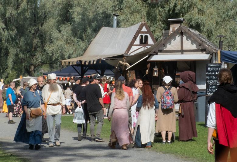 Kuvassa on vasemmalla on pariskunta kävelemässä vastaan. Naisella on siniharmaa mekko ja miehellä vaalea paita ja harmaat housut.  Toiseen suuntaan kävelee runsaasti väkeaä. Taustalla näkyy keskiaikaisen näköisiä rakennuksia. Edessä oikealla näkyy puna-musta paita.