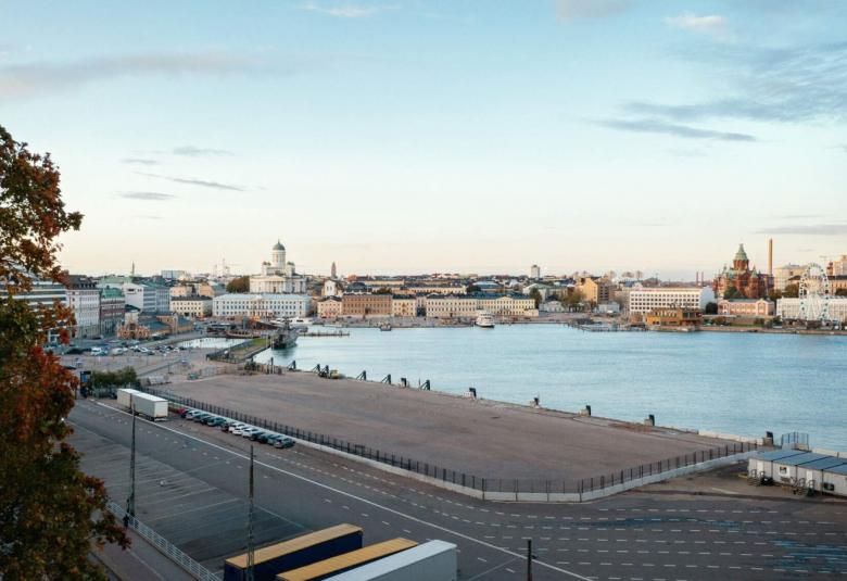 Kuvassa on taaempana Helsingin kauppatorin rakennukset ja edustalla näkyy sinistä merenlahtea.  Edessä on asfalttikenttää ja ylhäältä tulee leveät A-kirjaimen muodot tekevät palkit.