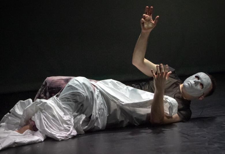 Kuvassa on Carl Knif lattialla ja hänellä on kädet ojennettuina pienessä kulmassa ylöspäin.  Hänellä on musta lyhythihainen t-paita ja valkoinen lakana kiedottuna puolen vartalon ja vasemman jalan ympäri. Kasvot on meikattu vaaleiksi. Tausta on musta.  